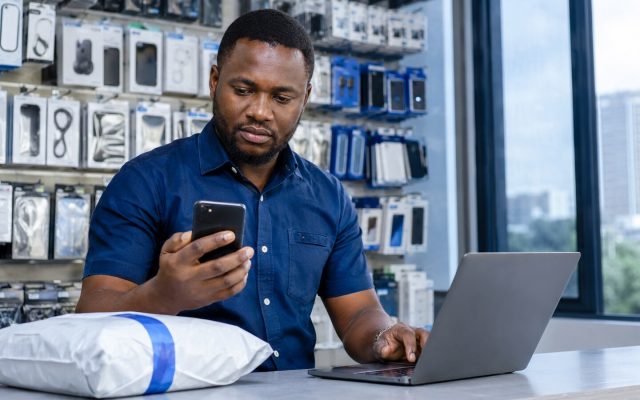 Nigerian shop owner checking a bank account before releasing an order