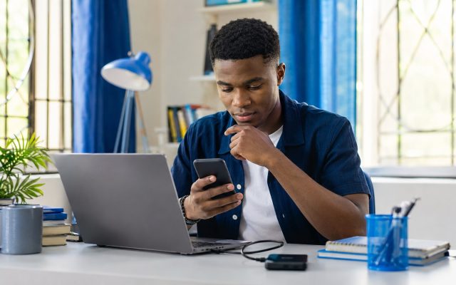 Nigerian student reviewing phone files beside a laptop and backup drive
