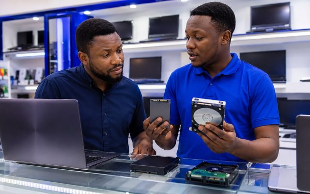 Nigerian laptop buyer comparing an SSD and hard disk with a technician