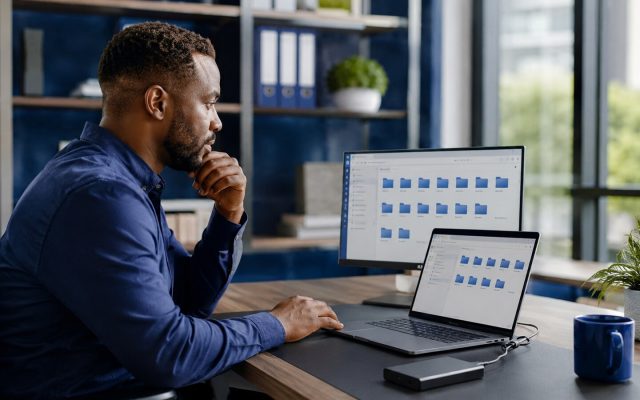 Nigerian business owner checking files on a laptop and external backup drive