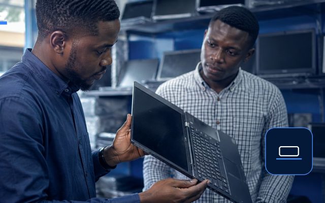 Two Nigerian shoppers inspecting a used laptop in an electronics store